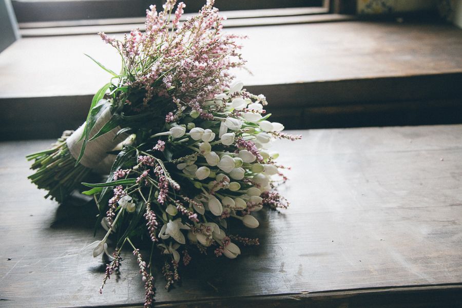 Romantic wedding bouquet with white tulips and pink wildflowers resting on a rustic wooden surface.