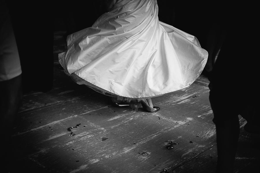 Black and white photo of a bride twirling her wedding dress on a wooden dance floor.