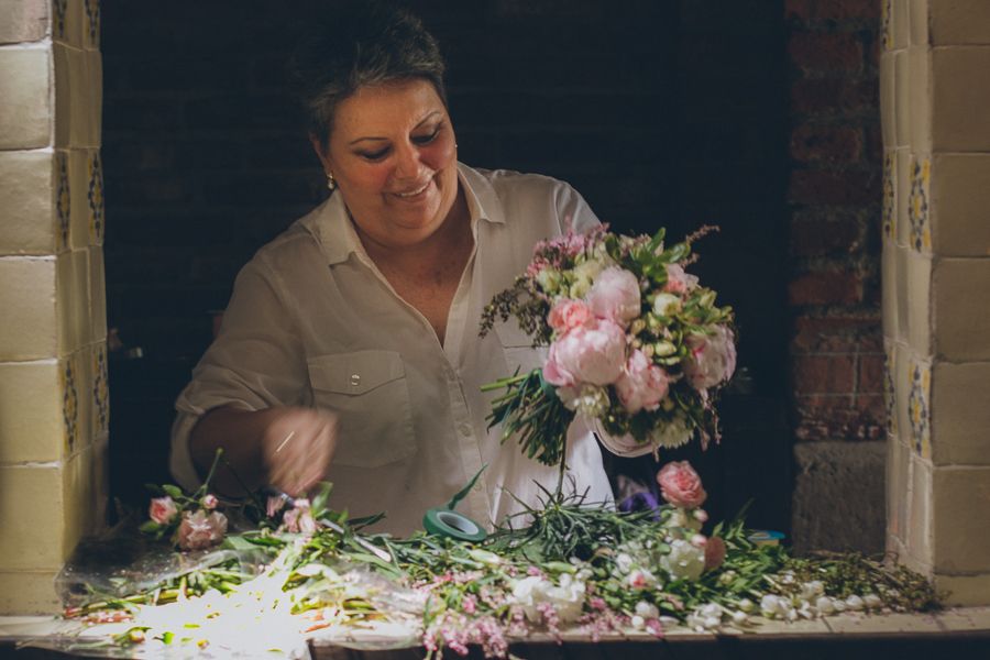 Florist arranging pink peony wedding bouquet on a rustic table with scattered petals.