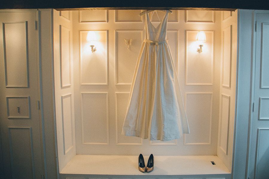 White wedding dress hanging in elegant closet with heels placed neatly below.