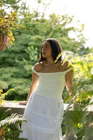 A white off-shoulder eyelet dress catches golden sunlight in a lush garden setting.