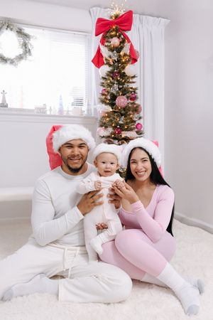 Family in matching white and pink outfits pose by decorated Christmas tree.