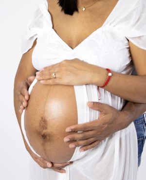 A maternity photo showing hands cradling a pregnant belly in a white dress.