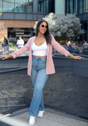 Casual spring outfit with pink blazer, white crop top and jeans worn while posing outdoors near blooming trees.