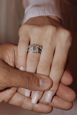 Close up of sparkly diamond engagement ring and wedding band on manicured hand.