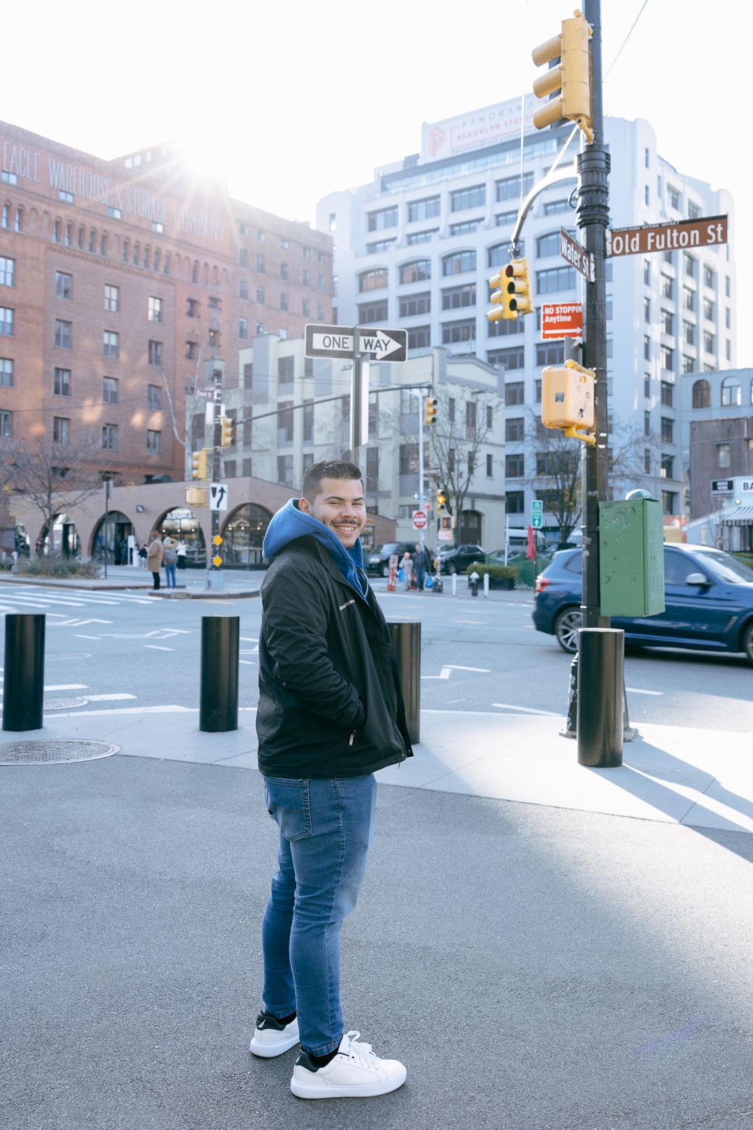 Person standing on NYC street corner with buildings and traffic light in background.