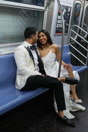 Couple in white formal wear share a joyful moment while riding together on the subway.