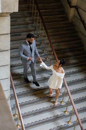 A couple in formal attire dancing on an elegant staircase with wooden steps and brass railings.
