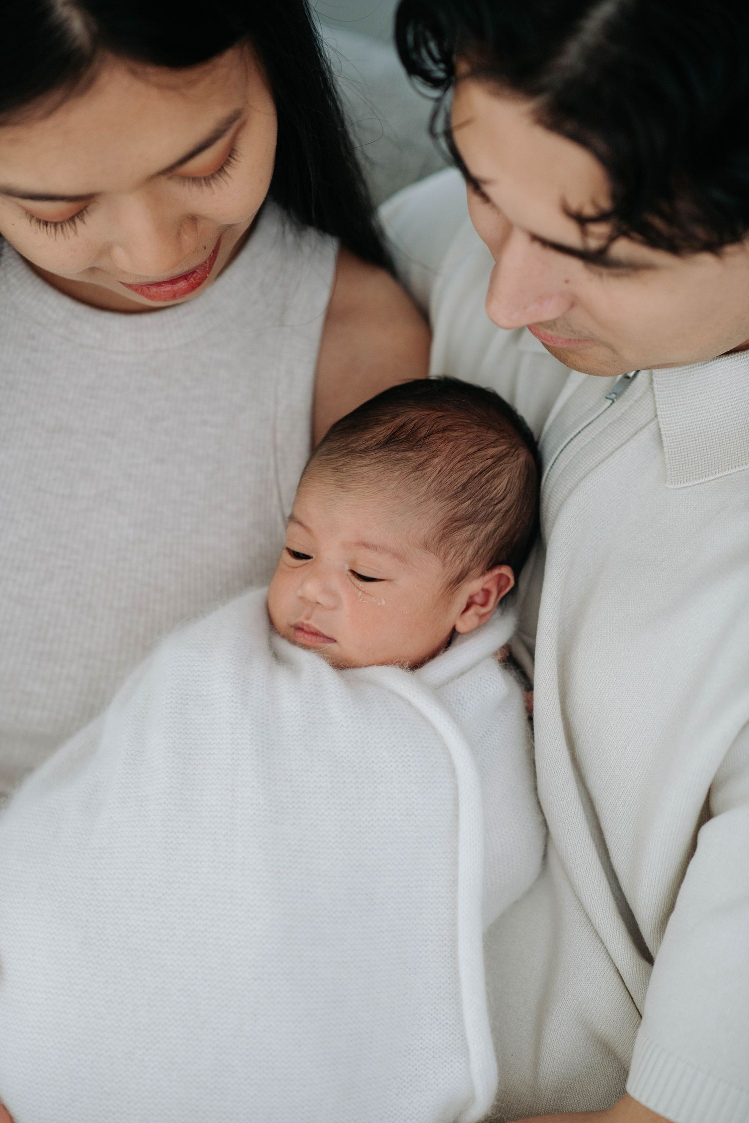 Intimate family moment with sleeping newborn wrapped in white blanket.