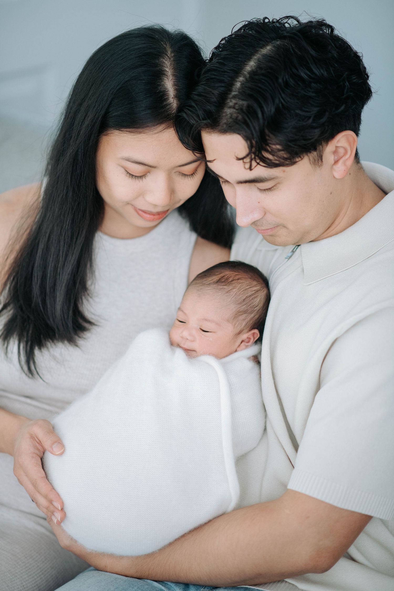 Parents sharing tender moment with newborn baby wrapped in white blanket.