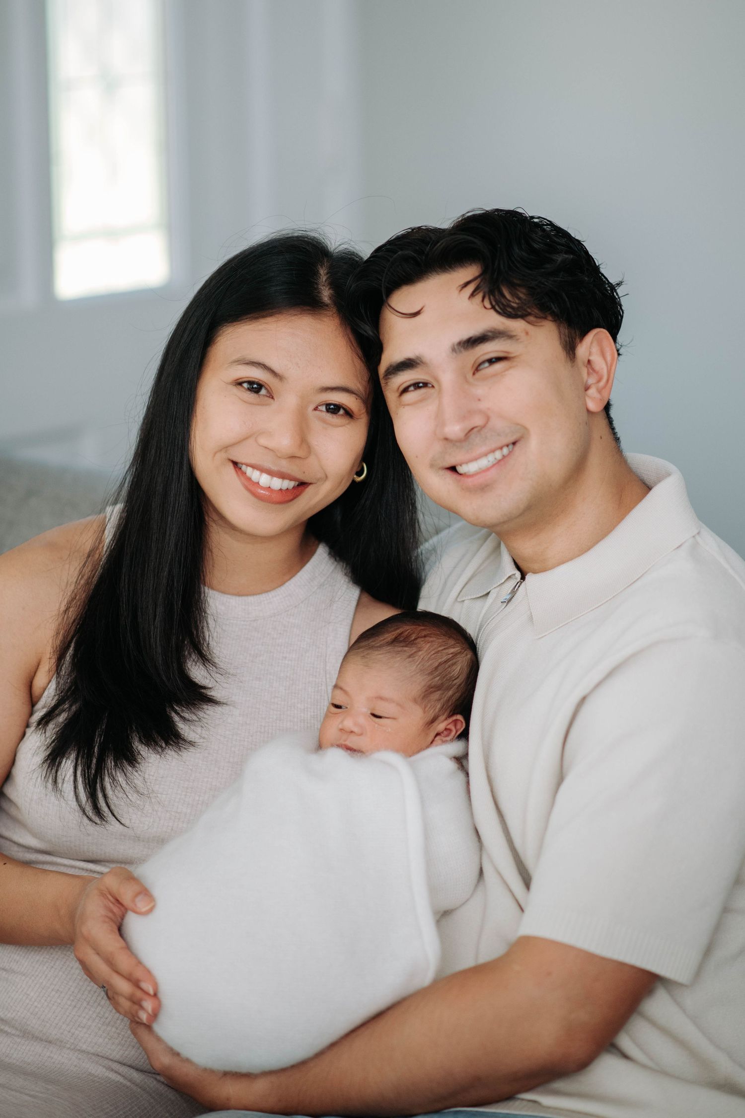 Family portrait on grey sofa with newborn baby in minimal studio setting.