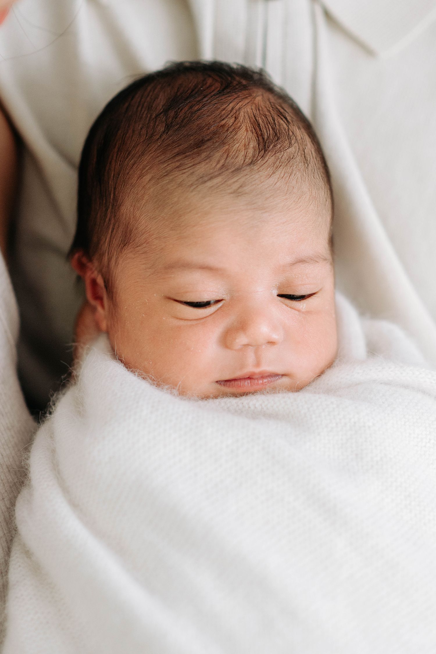 Close-up of peaceful sleeping newborn baby wrapped in white blanket.