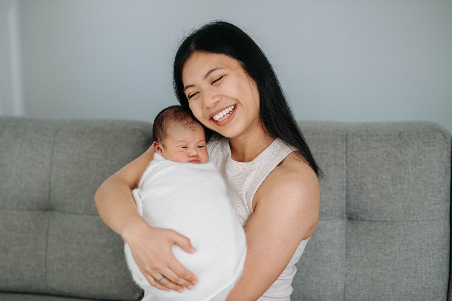 A tender moment between a caregiver and sleeping newborn baby on a grey couch.