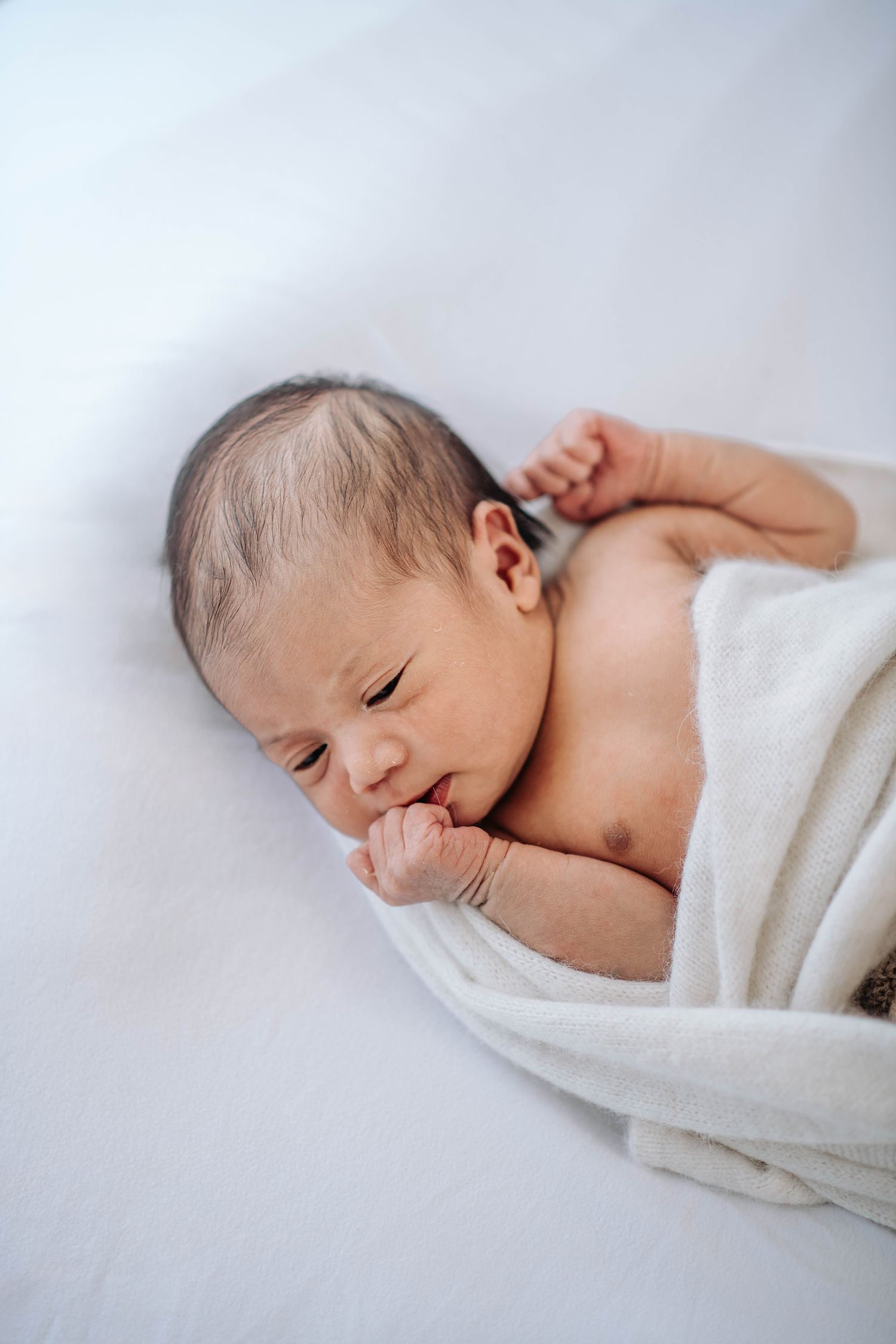 Peaceful sleeping newborn baby wrapped in soft white blanket.