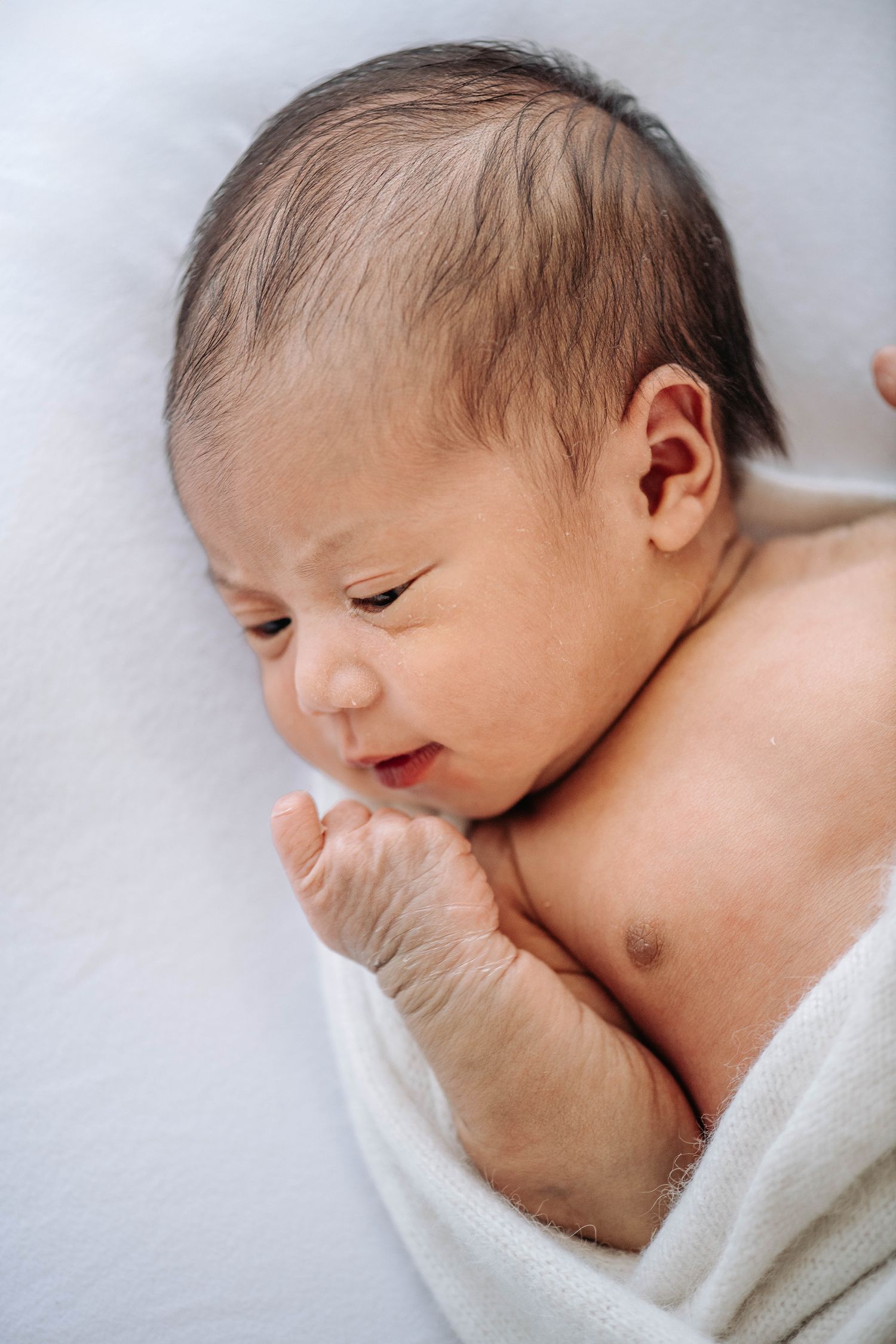 Sweet newborn baby wrapped in white blanket making expressive faces.