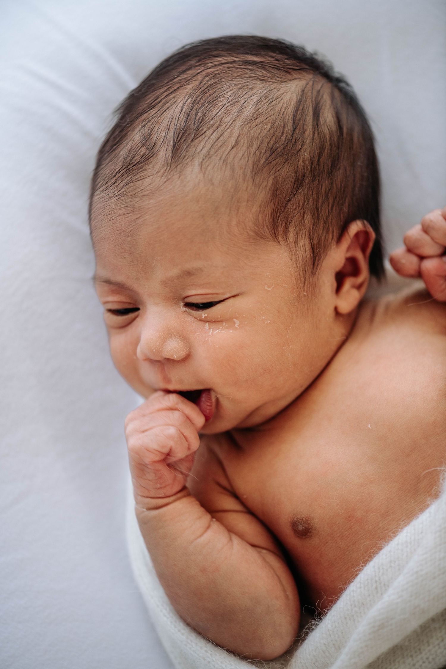 Adorable newborn baby with a gummy smile sucking their thumb.