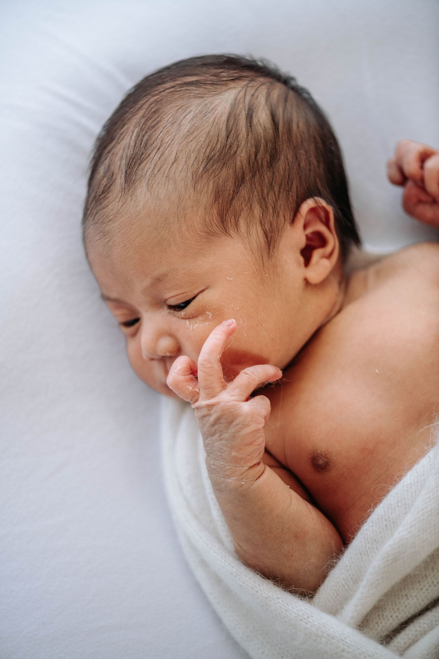 Close-up of a newborn resting peacefully against white bedding.