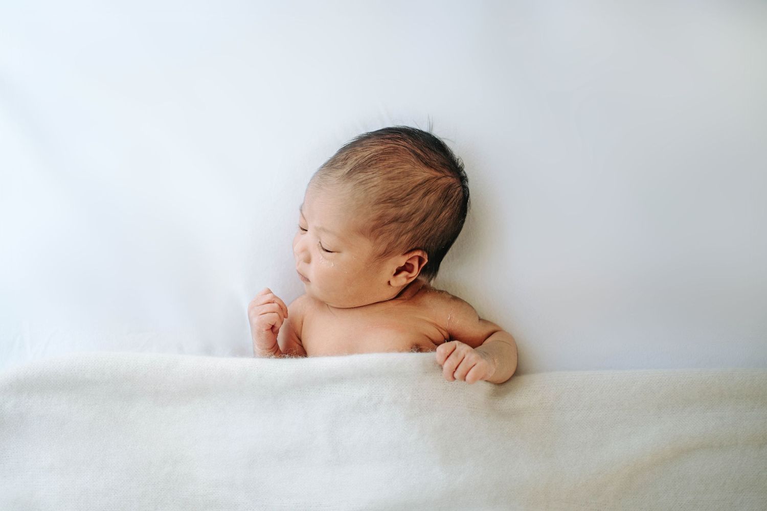Serene newborn baby resting on white bedding.
