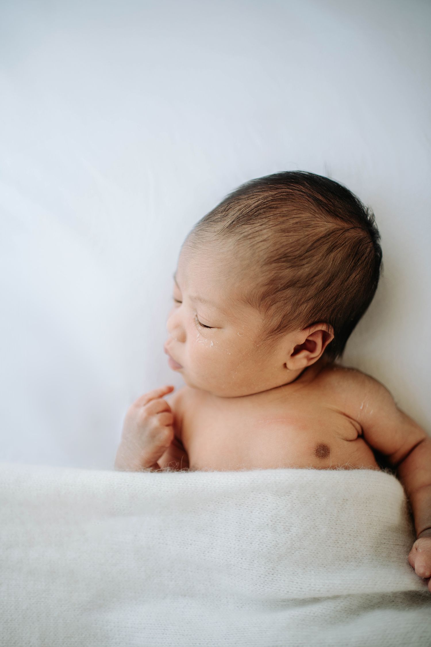 Side view of peaceful newborn baby lying on white bedding.