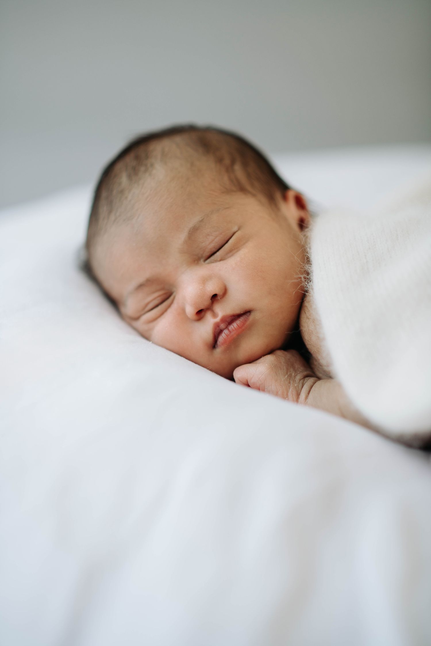 Close-up of sleeping newborn resting peacefully on white bedding.
