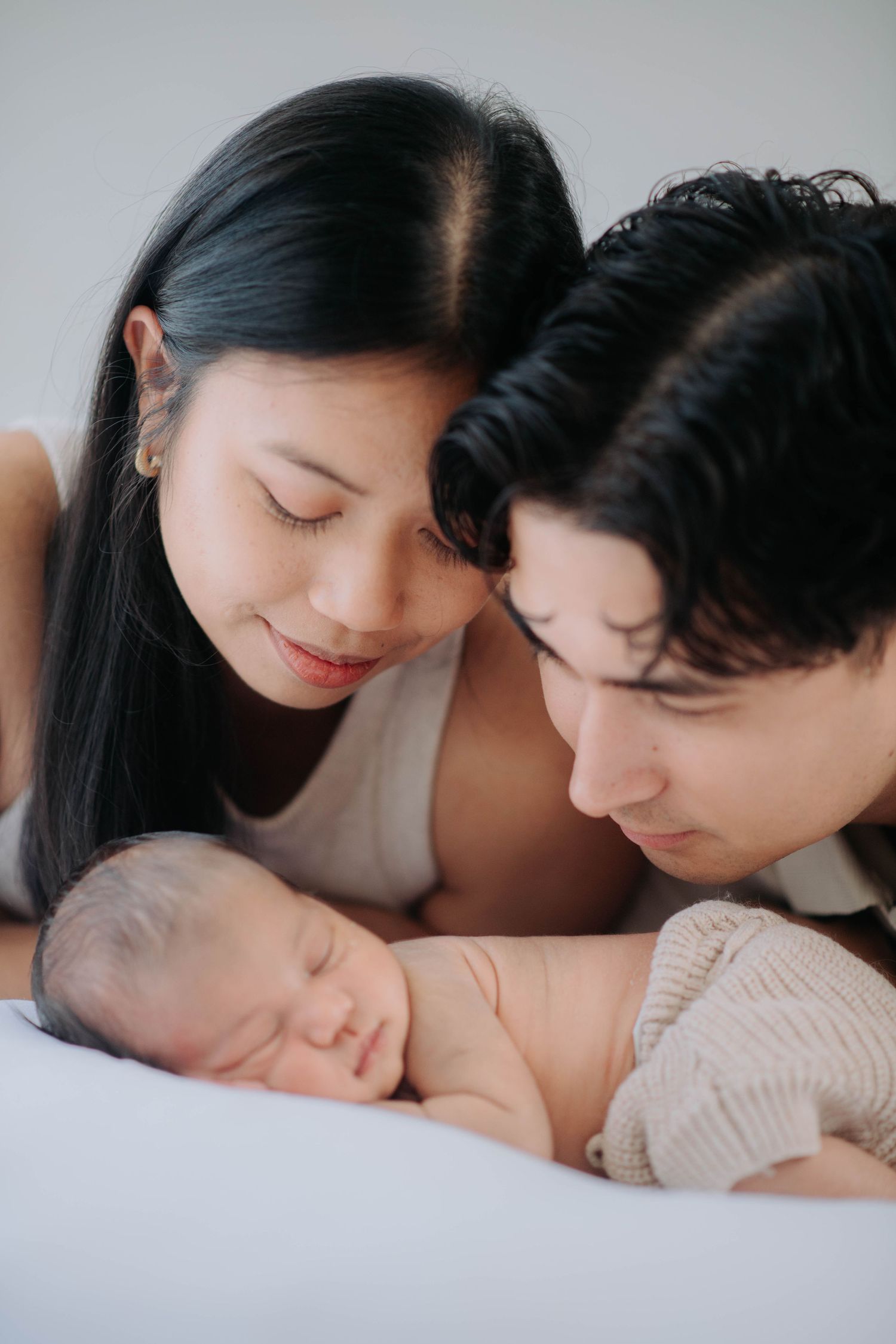 Parents lovingly watching their sleeping newborn on white bedding.