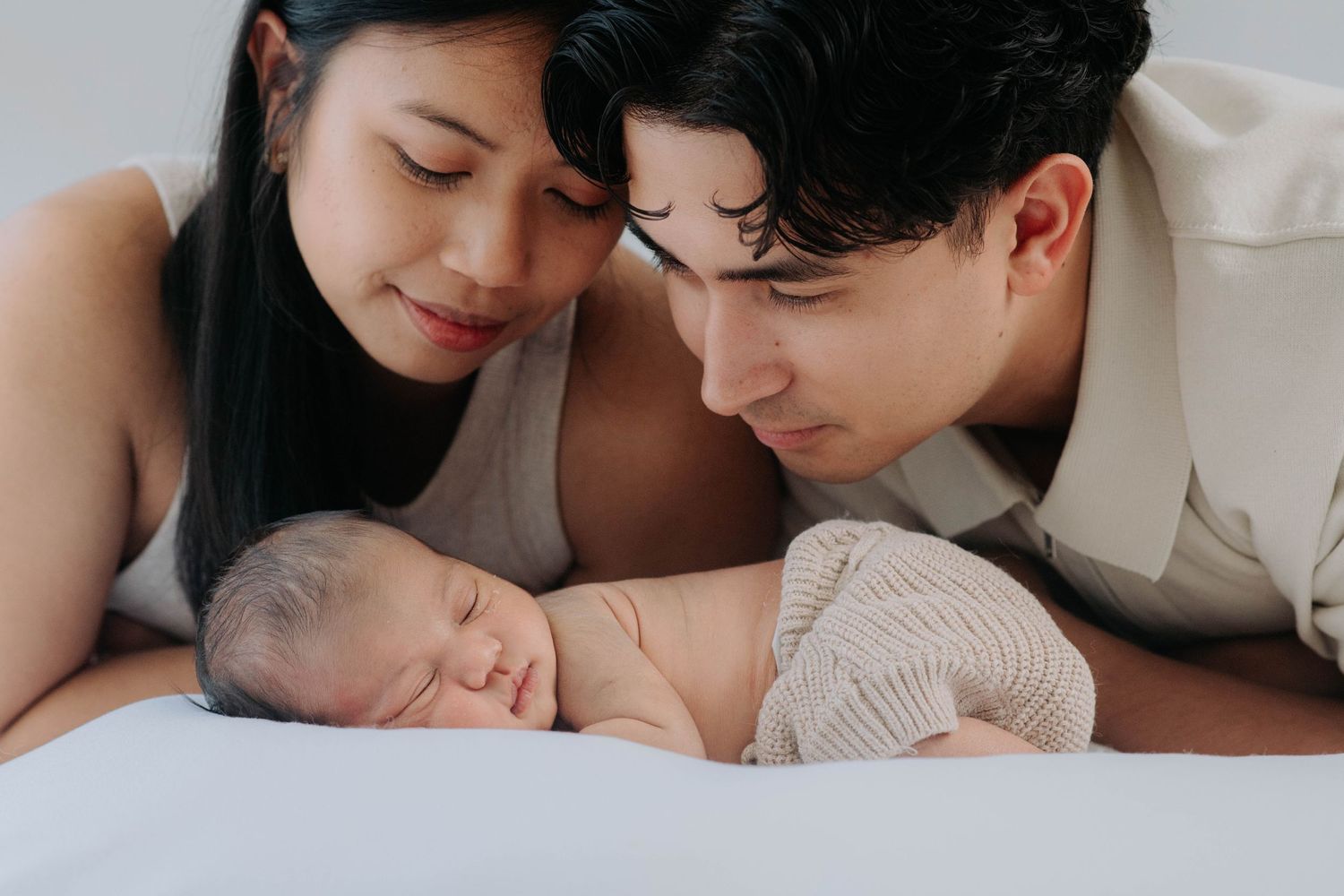 Family sharing intimate moment with sleeping newborn on white surface.