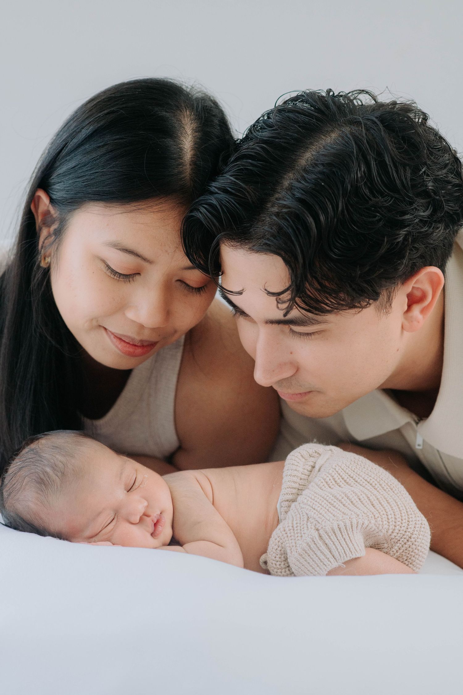 Family gazing lovingly at sleeping newborn wearing knit bottoms.