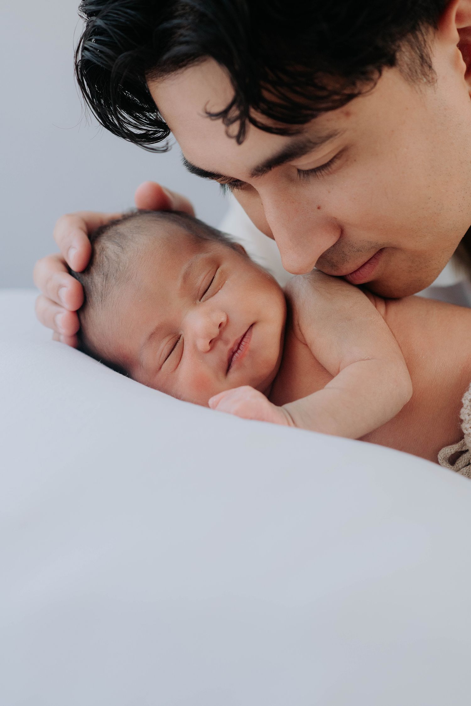 Intimate close-up of parent with sleeping newborn on white bedding.