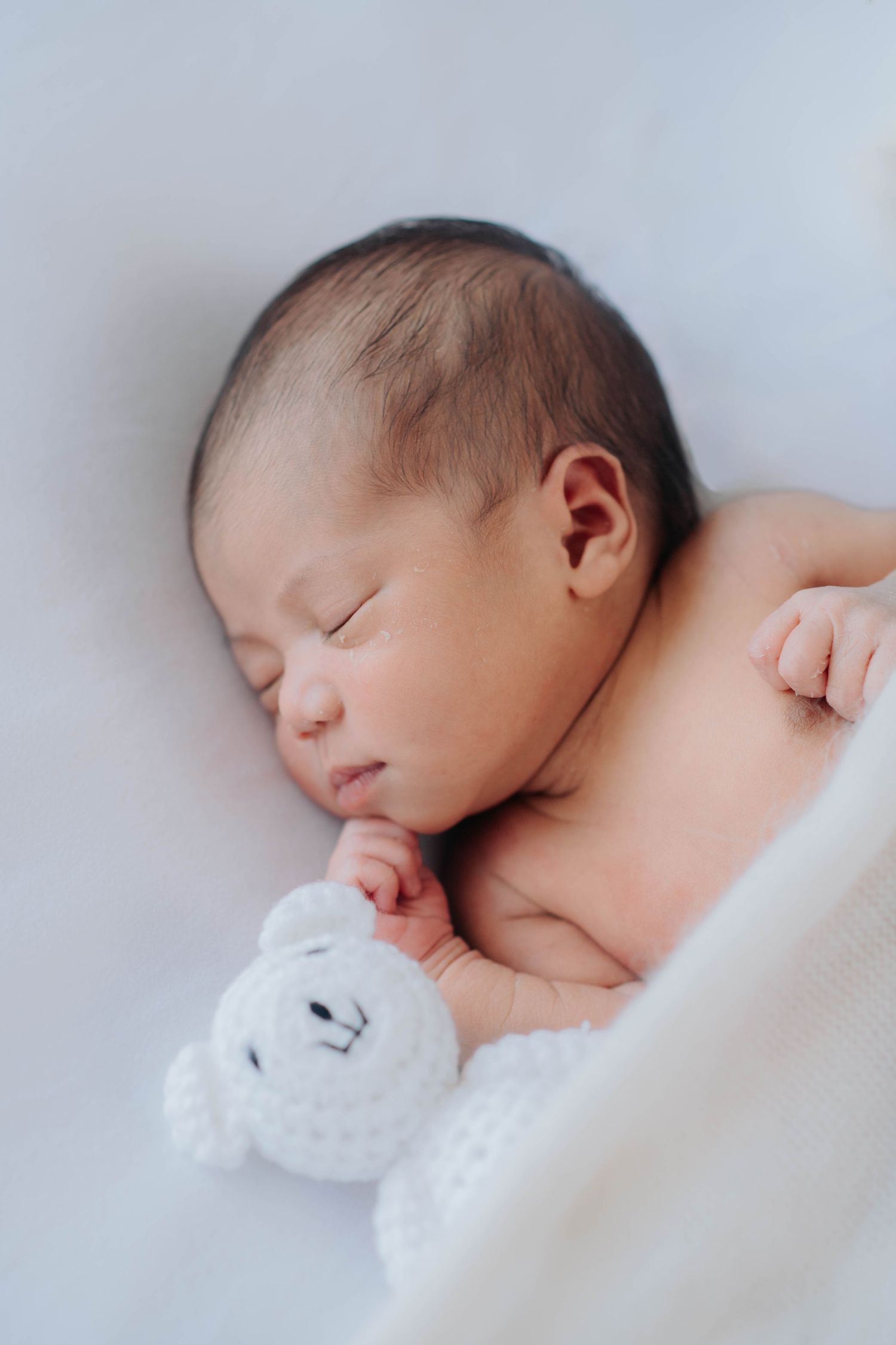 Sleeping newborn holding small stuffed toy while resting on white blanket.