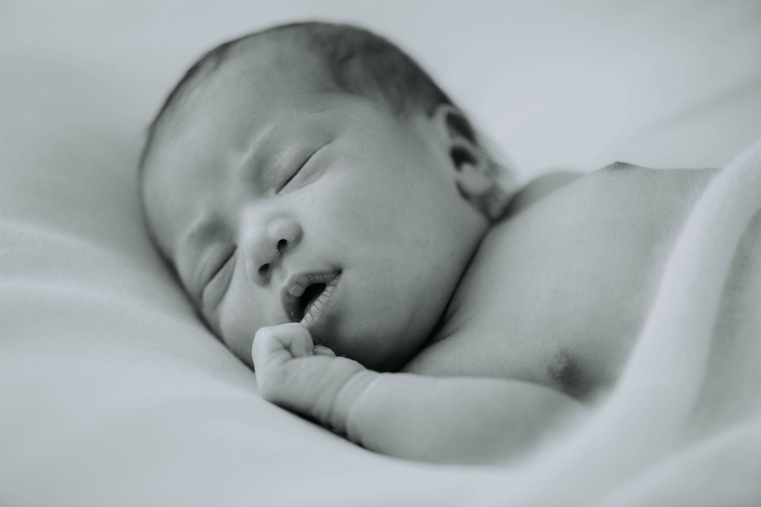 Black and white portrait of a sleeping newborn with hand near face.