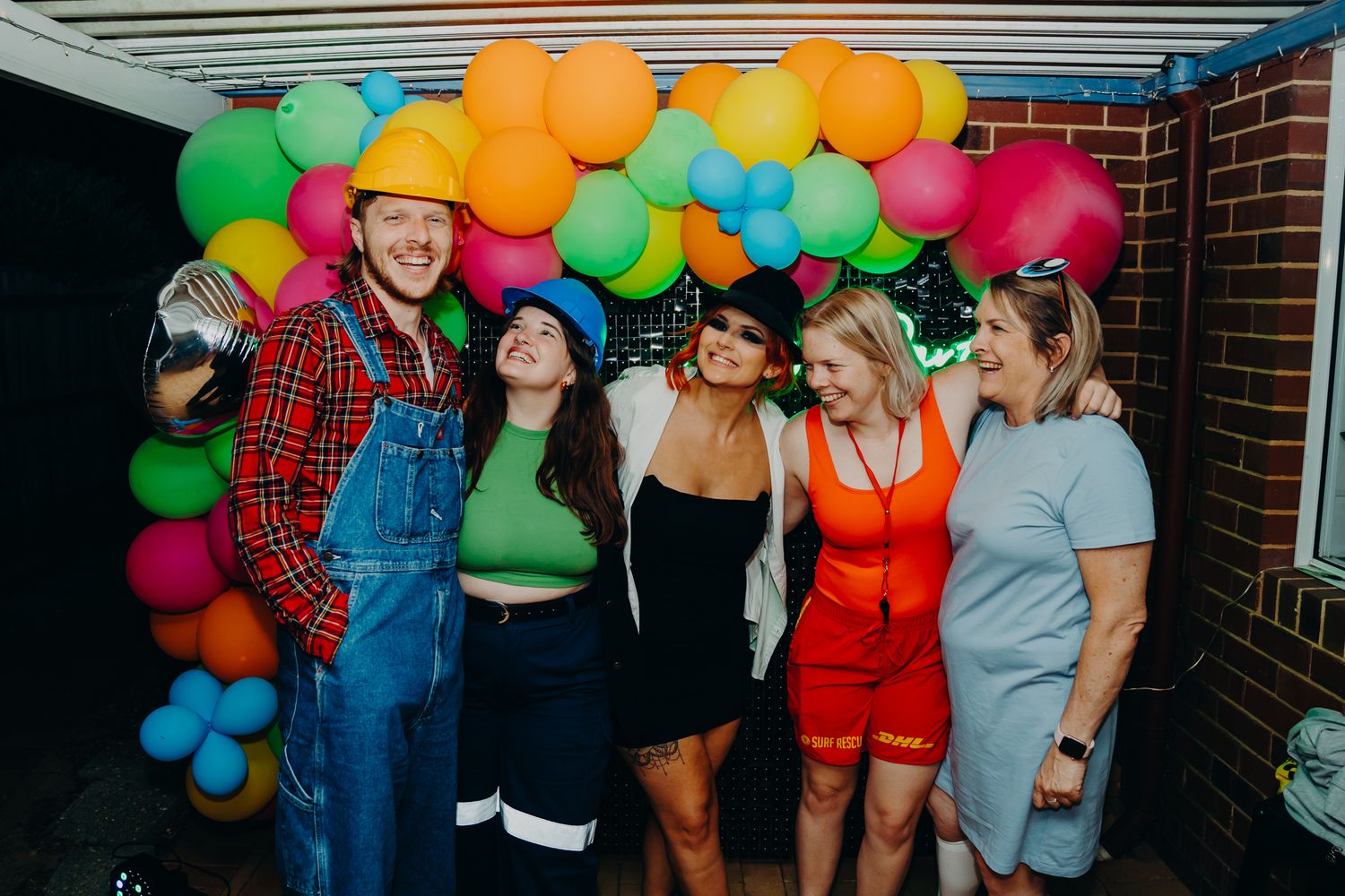 Group celebrating under colorful balloon garland at night.