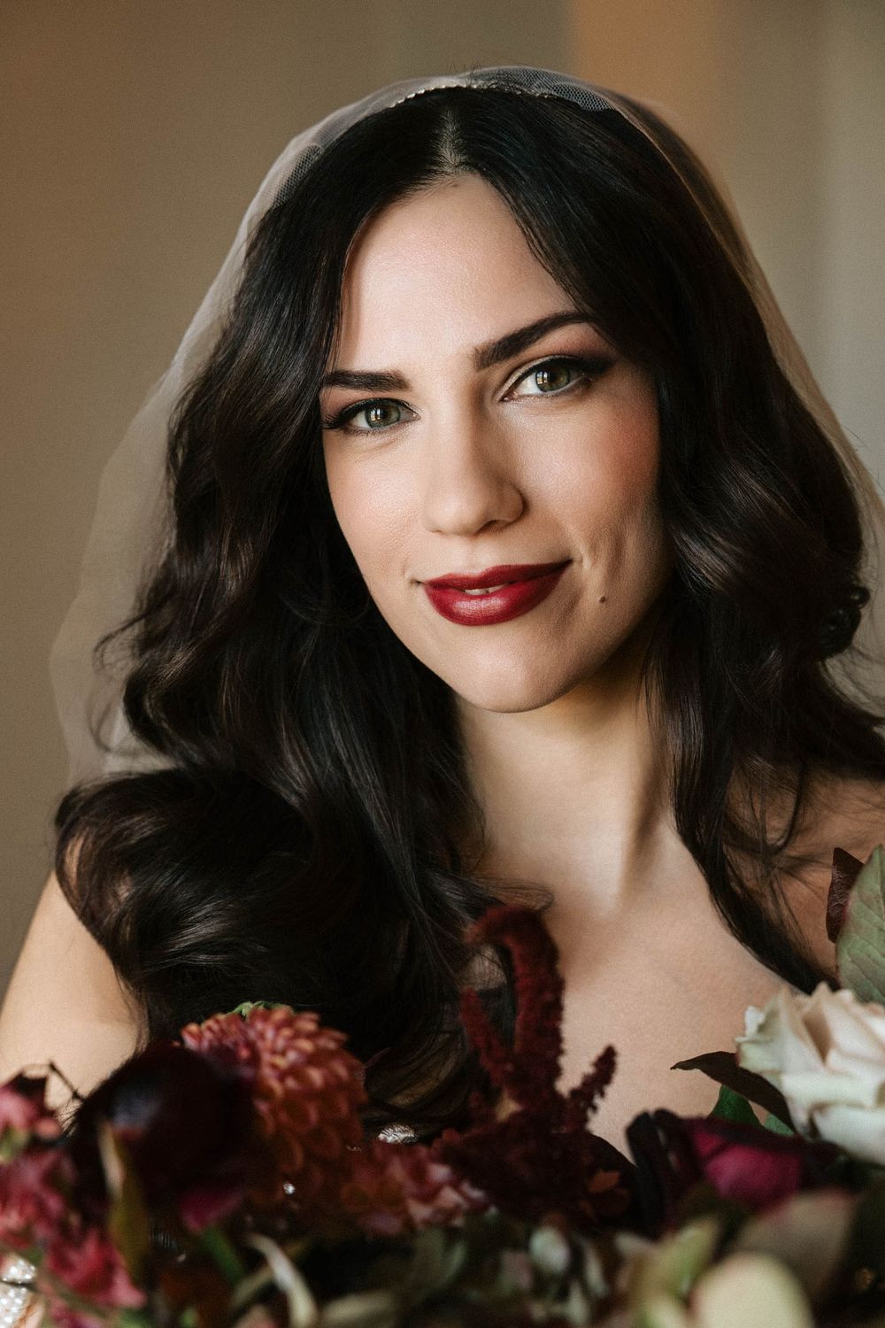 Romantic beauty portrait with dark wavy hair, red lipstick and floral arrangements in warm tones.