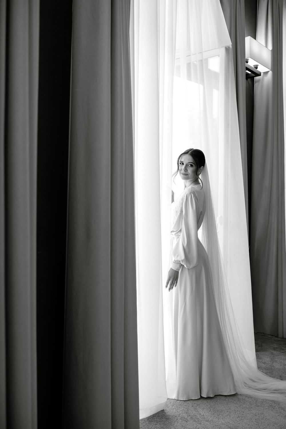 Dramatic black and white bridal portraits showing a flowing white wedding dress against curtained windows.