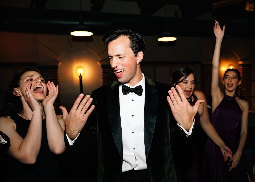 People in formal attire laugh and gesture expressively during what appears to be an elegant evening event.