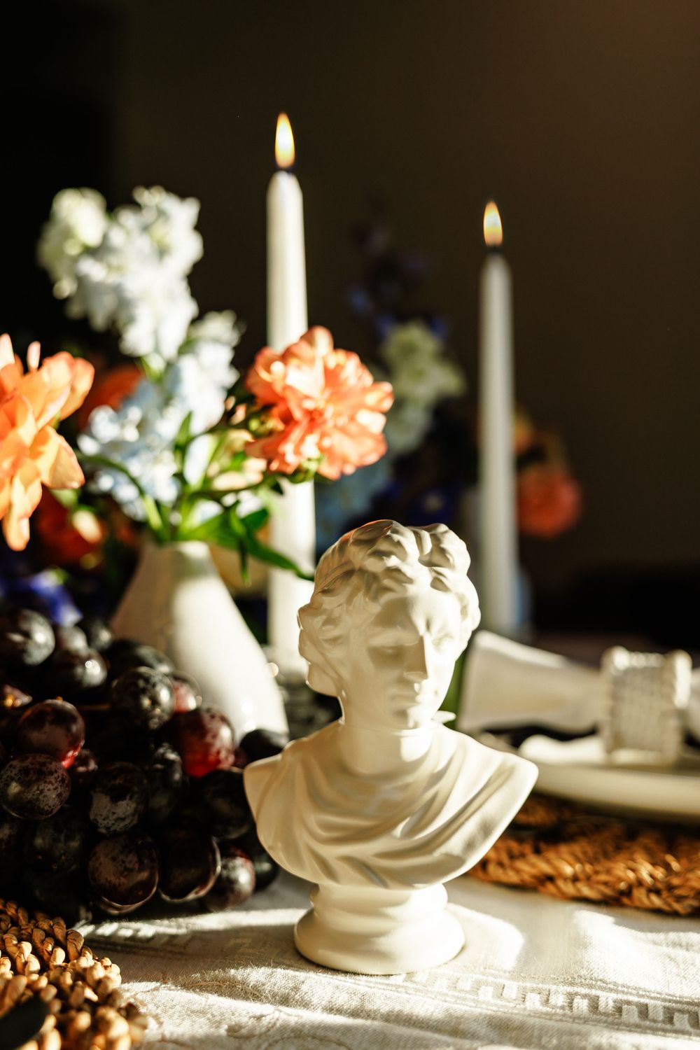 A white cherub statue sits on an elegant table setting with lit candles and floral decorations in soft lighting.