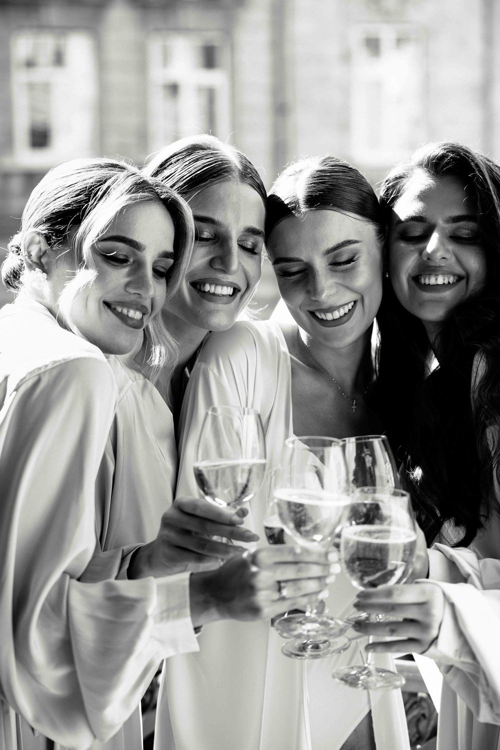 A group of people in white outfits smile and laugh together while holding wine glasses in a celebratory moment.