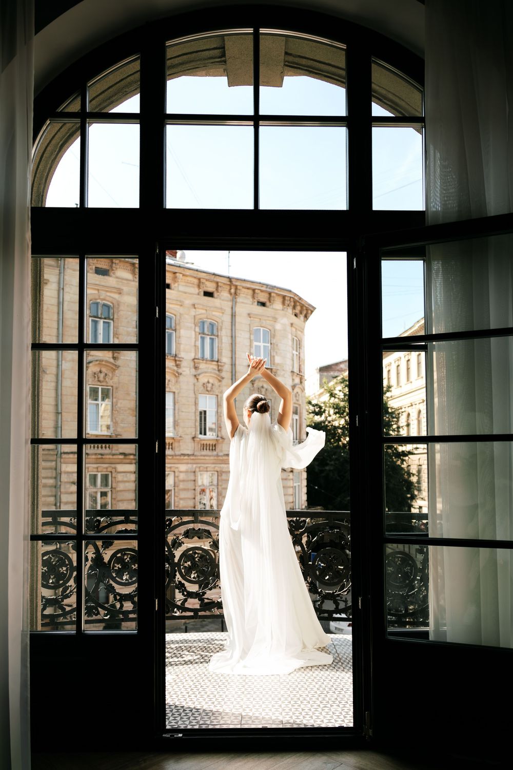A wedding dress hangs elegantly in front of large windows overlooking historic architecture and buildings.