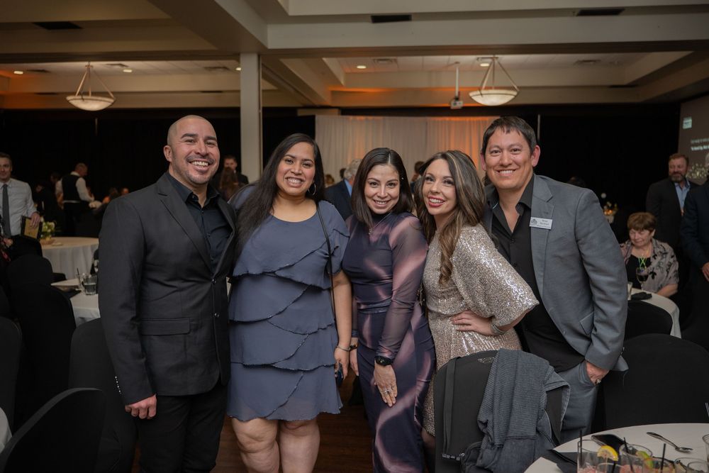 Five people smiling and posing together at a formal banquet event in an elegant venue.