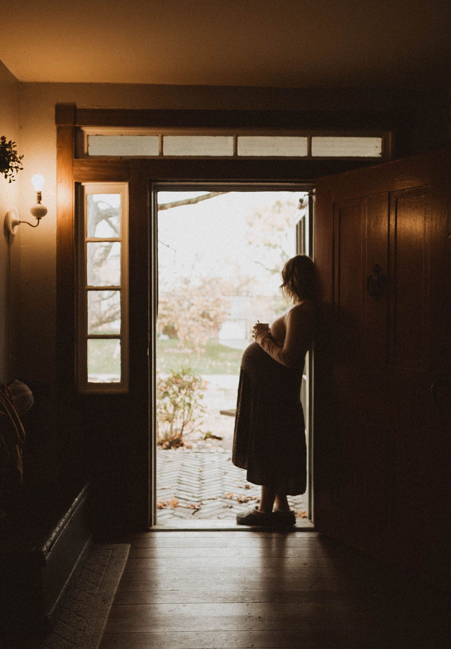 Silhouette of person standing in doorway holding a cup during warm sunset light.