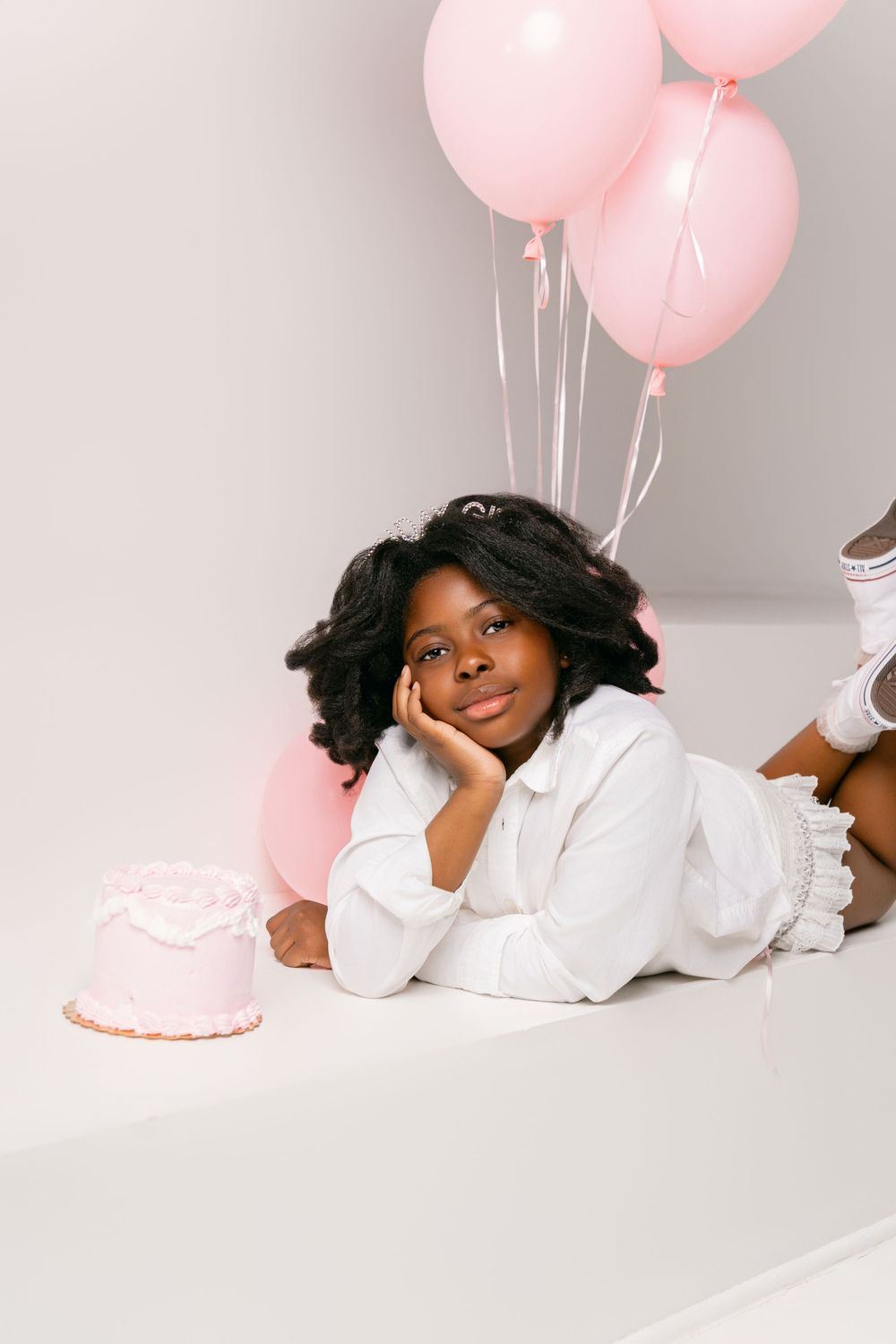 Pink birthday setup with balloons and cake against white backdrop for portrait photography session.