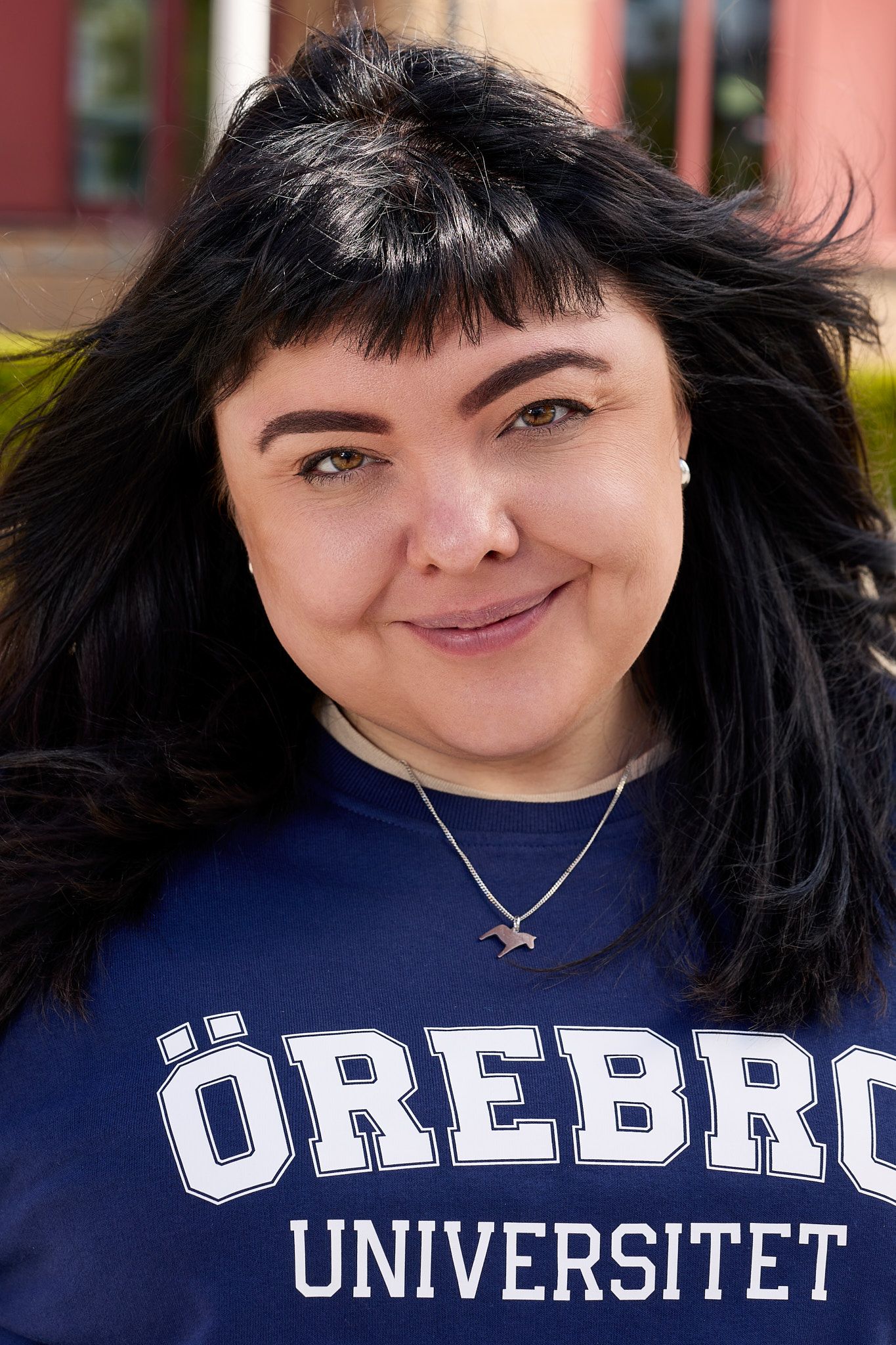 Student wearing a navy blue Örebro Universitet sweatshirt and silver necklace smiles at camera.