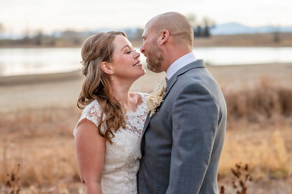 Bride and groom share a romantic moment outdoors with golden fields and mountains in the background.