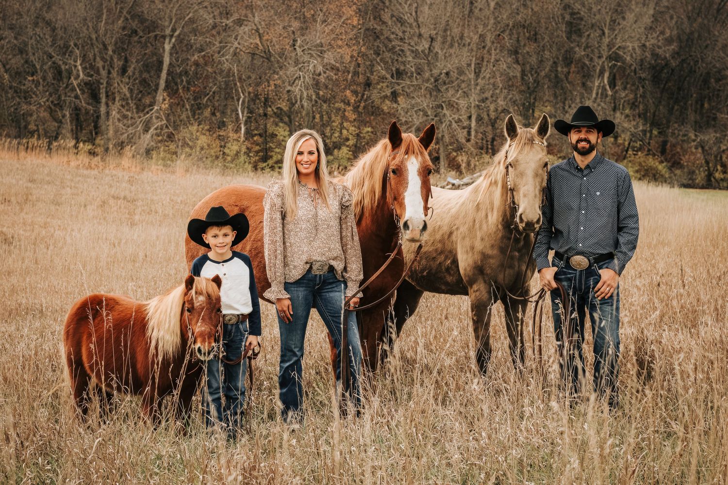 Family standing with horses in tall grass field during golden hour.