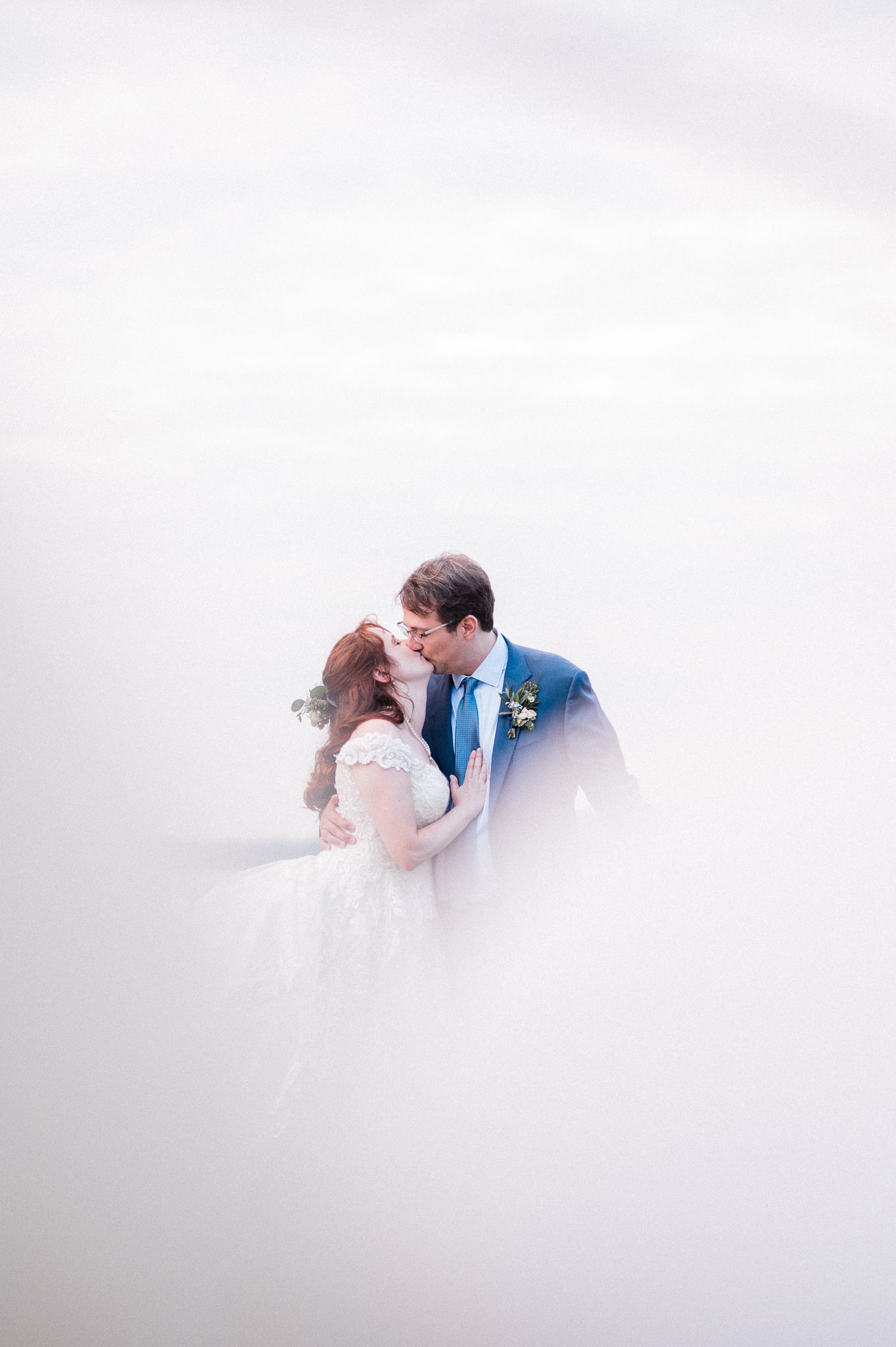 A romantic wedding couple shares an intimate moment surrounded by soft ethereal fog during their outdoor photoshoot.