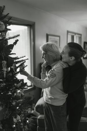 Black and white images show people decorating a Christmas tree together in sequence.
