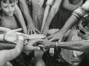 Black and white close-up of many hands joining together in a circle.