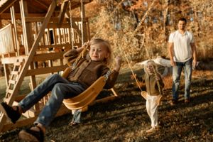 Children playing on a backyard swing set during golden hour with fall foliage in the background.