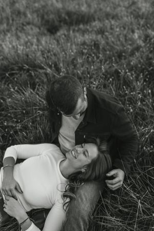 Intimate black and white portrait of a couple laying in tall grass.