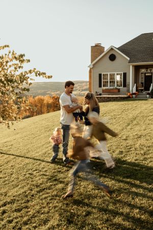 Family playing together on a grassy hill outside their home at sunset.