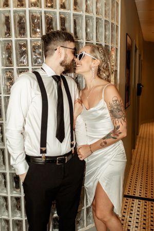A romantic couple in wedding attire sharing an intimate moment against a glass block wall.